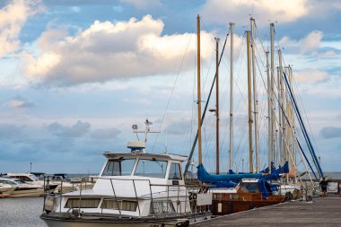 Limanı rıhtımdaydı. Birçok yat demirlemişti. Gökyüzü bulutluydu ve arka planda günbatımı vardı..