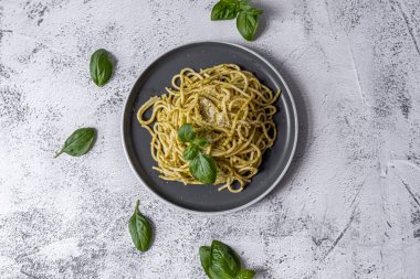 Pesto soslu makarna ve gri kasede taze fesleğen yaprağı. Açık gri arkaplan. Üst Manzara. Yüksek kalite fotoğraf