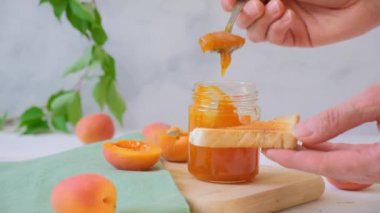 Kavanozda kayısı reçeli. Bir kadının eli tostun üstüne kayısı reçeli sürer. Yüksek kaliteli FullHD görüntüler
