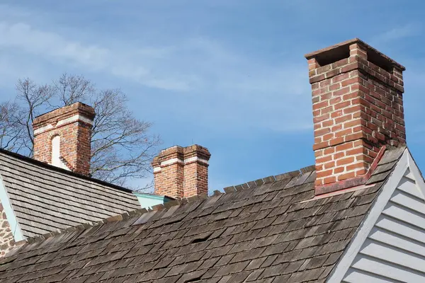 There are 3 chimneys on the rooftops on a cold afternoon.
