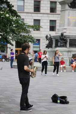 Genç adam saksafonunu çalıyor ve insanların kutuya para koymasını umuyor..