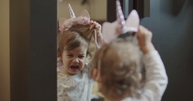 Bebek kız aynada kostümüne bakıyor ve ondan nefret ediyor. Komik, gerçek hayat klipsi. 4K RAW 'da bir sinema kamerasında çekildi..