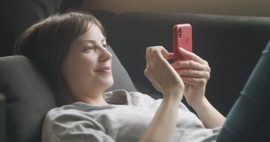 Kanepede mobil cihazını kullanan bir kadın. 4K RAW 'da bir sinema kamerasında çekildi..