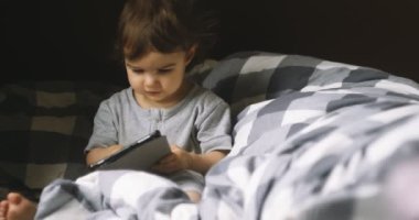 Yatakta tablet kullanan bir yaşında bir kız. Sinematik 4K görüntüleri.