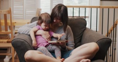 Anne ve kızının bir kanepede birlikte kitap okuduğu yakın plan. Sinematik 4K Görüntü.