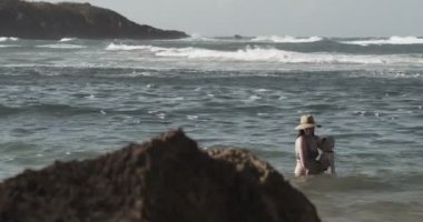 Anne ve bebek kumsalda eğleniyorlar. 4K 'de bir sinema kamerasında çekildi. Kaydırıcı atışı.