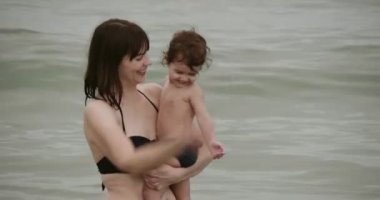 Anne ve bebek kumsalda eğleniyorlar. 4K 'de bir sinema kamerasında çekildi. Kaydırıcı atışı.