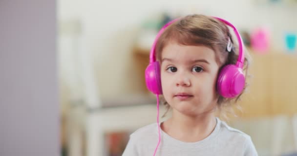 蹒跚学步的女孩戴着粉色耳机 欣赏着音乐 被电影摄影机拍到 — 图库视频影像