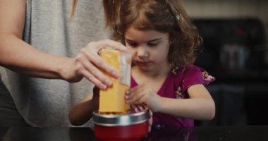 Küçük kız peynirli makarna yapmaya yardım ediyor. 4K 'da bir sinema kamerasında çekildi..