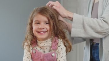 Anne yeni yürümeye başlayan kızların saçlarını tarıyor. Gülümseyen mutlu aile konsepti.