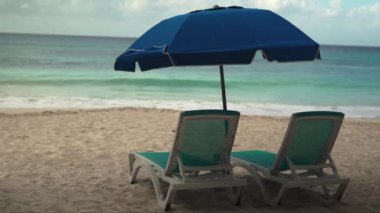 Huzurlu bir kumsal. İki boş sandalye ve bir şemsiye. Huzurlu okyanusa davetkar bir şekilde bakıyor. Sessizliği ve rahatlatıcı kaçışları tasvir etmek için mükemmel.