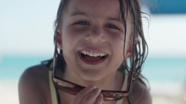 5 yaşındaki bir kızın kumlu bir plajda eğlenip gülümseyip kaygısız bir çocukluk yazının özünü yakaladığı iç açıcı bir sahne.