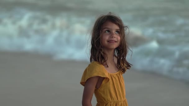捕捉到一个5岁的女孩在黄昏时在海滩上微笑时的纯粹喜悦 背景中柔和的波浪翻滚在岸边 温馨的场面 — 图库视频影像