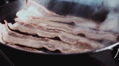 Dökme demir tavada cızırdayan domuz pastırmasının 4K görüntüsü. Yemek reklamları, yemek programları ve restoran tanıtımları için ideal..