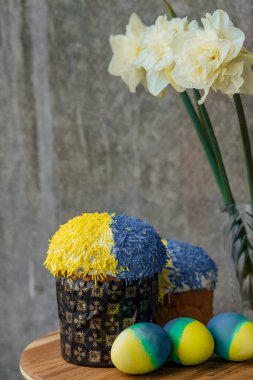 Ukrayna bayrağının renginde lezzetli Paskalya pastaları, arka planda çiçekler olan ahşap bir masada sarı-mavi Paskalya yumurtaları. mesaj için yer. seçici odak.