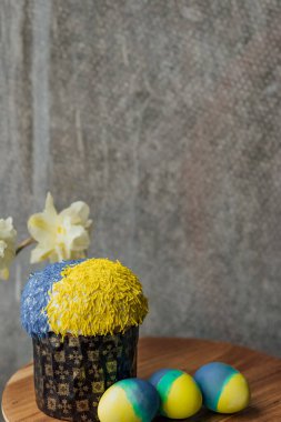 Ukrayna bayrağının renginde lezzetli Paskalya pastası, arka planda çiçekler olan ahşap bir masada sarı-mavi Paskalya yumurtaları. mesaj için yer. seçici odak.