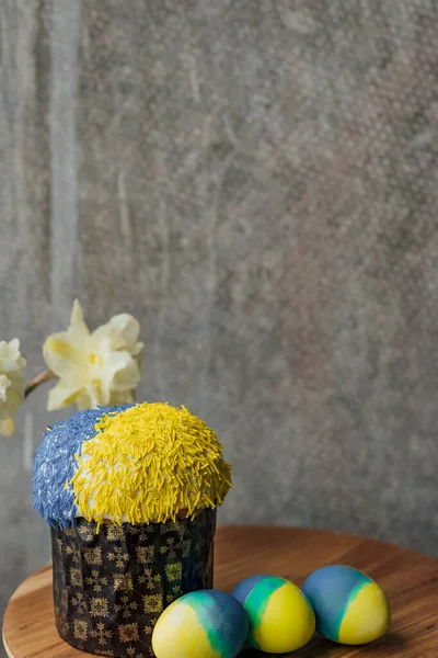 Delicious Easter cake in the colors of the flag of Ukraine, yellow-blue colored Easter eggs on a wooden table with flowers in the background. place for text. selective focus.