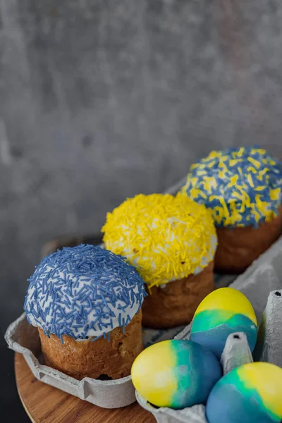 Easter cakes in the colors of the flag of Ukraine, yellow and blue in a cardboard stand with eggs, Easter eggs. place for text. selective focus.