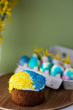Paskalya kompozisyonu, sarı-mavi Paskalya pastaları, serpiştirmeler, Paskalya yumurtaları. Ahşap tezgah ve sarı arka planda bahar çiçekleri. Boşluğu kopyala.