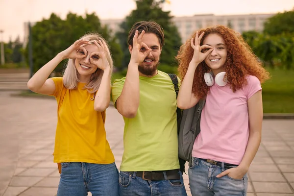 快乐的男人和女人穿着五颜六色的T恤衫 近着眼睛摆出一副不错的姿势 微笑着看着相机 同时还在大学后的公园里呆着 — 图库照片