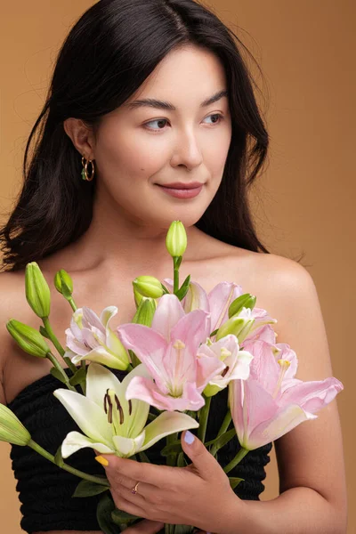 Asian female model with bunch of natural lilies looking away against brown background