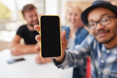 Arkadaşların ve reklam uygulamalarının yanında otururken siyah ekranlı cep telefonu sergileyen siyahi erkeğin yumuşak odağı
