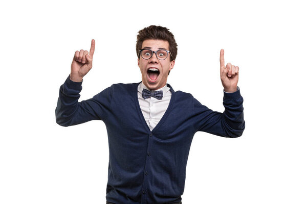 Happy young man in smart casual clothes and glasses looking at camera with opened mouth and pointing up against white background