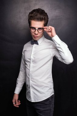 Kendine güveni tam, şık giyinmiş dudaklarını büzen ve siyah arka plana karşı gözlük takan genç bir adam.