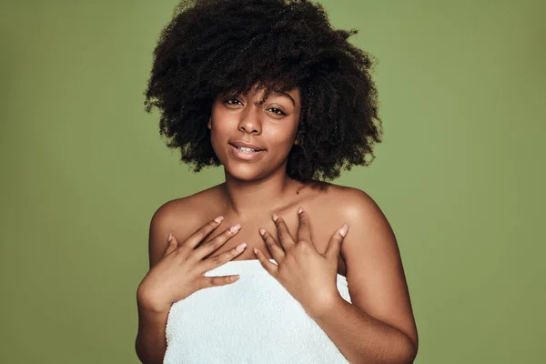 年轻的非裔美国女性 裹着白毛巾 卷曲的头发 触摸着胸部 在皮肤护理的过程中 在绿色背景下看着相机 — 图库照片