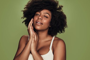 Beyaz elbiseli, kıvırcık saçlı, yumuşak tenli ve yeşil arka planda gülümseyerek kameraya bakan siyah kadın.
