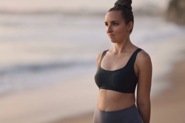 Aktif kıyafetli genç bir kadın okyanusla birlikte arka planda çalışırken ısınıyor.