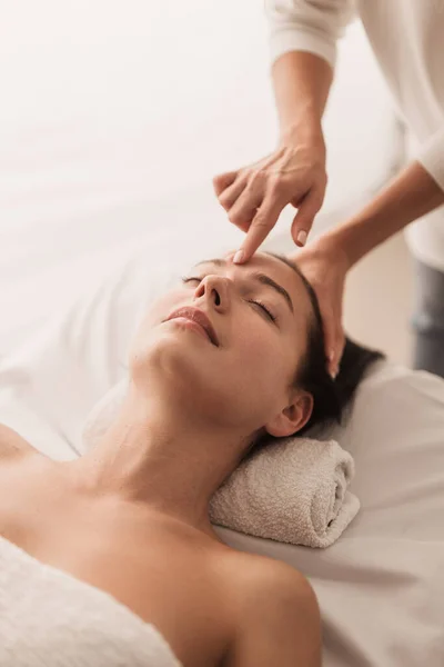 Crop massage specialist in acupuncture traditional medicine pressing point on head of calm woman lying on table