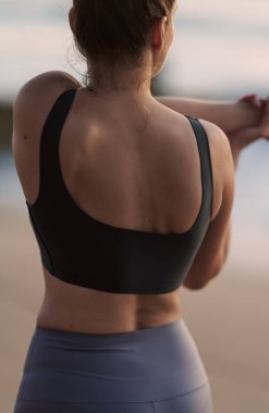 Back view of anonymous fit lady doing shoulder stretch to relieve pain in arms while standing in nature