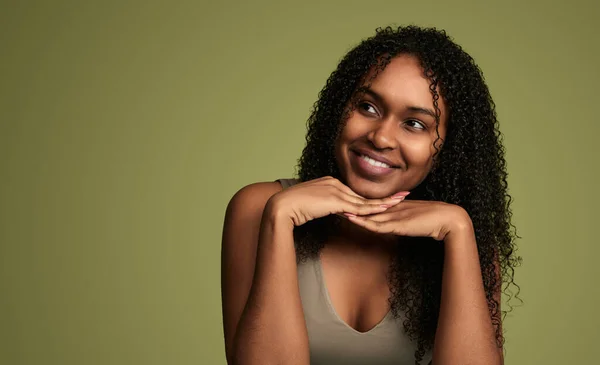 young cheerful african american woman with clean skin smiling and looking to the side at copy space in studio, isolated on green background. Concept of natural beauty and skincare