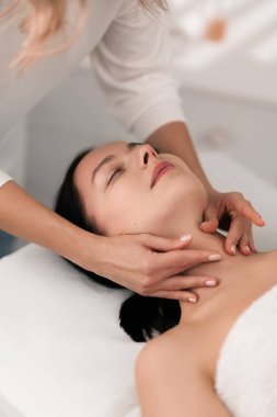 Bayan müşterinin boynuna nazikçe masaj yapan, modern ışık spa salonundaki rehabilitasyon seansında gözleri kapalı yatan, tanınmayan bir terapistten.
