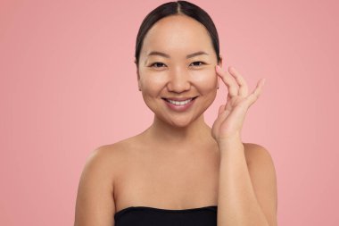 Çıplak omuzlu, makyajsız, yüzü pürüzsüz ve kameraya bakan neşeli, genç Asyalı bayan.