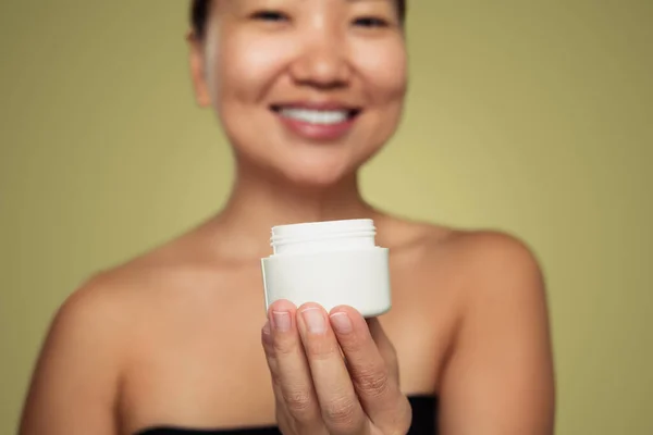 浅谈绿色背景下笑着的亚洲模特手中的白色空白奶油罐 — 图库照片