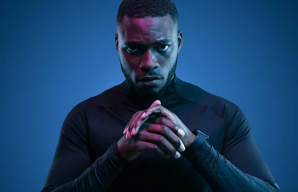有决心的非洲裔美国运动员 身穿黑色运动衫 双手交叉地站在黑暗的房间里 有霓虹灯 望着镜头 — 图库照片