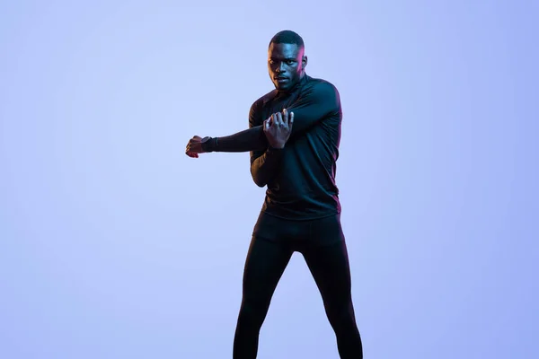 美国黑人男子运动员在霓虹灯演播室锻炼时 身穿黑色运动服的年轻而自信的 肌肉发达的黑人男子运动员张开双臂 — 图库照片