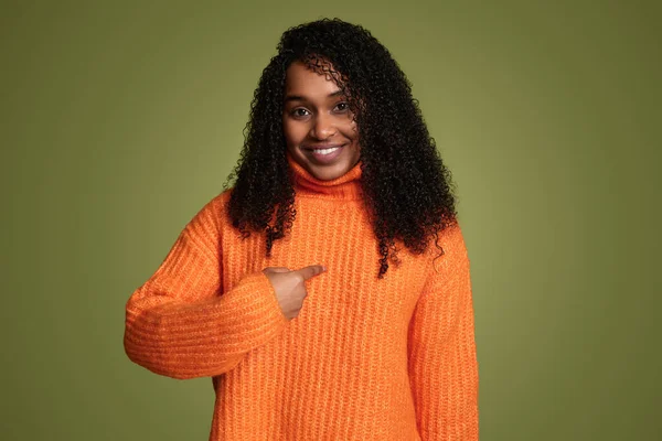 穿着鲜活的橙色毛衣 卷曲的头发 食指指向绿色背景的非洲裔美国女人 — 图库照片