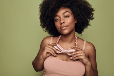 Afro saç stili ve pembe uyku maskeli genç Afro-Amerikalı kadın yeşil arka planda kameraya bakıyor.