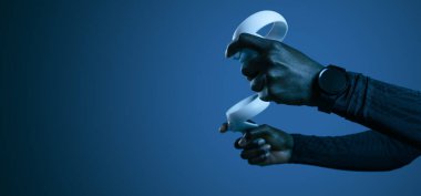 Mavi arkaplana karşı video oyunu oynarken modern beyaz VR denetleyici kullanan tanınmayan Afrikalı Amerikalı erkek oyuncu