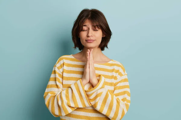 青い壁の近くに立っている黄色の縞模様のセーターで短い髪を持つ穏やかな若い女性と瞑想とともに閉じた目 — ストック写真