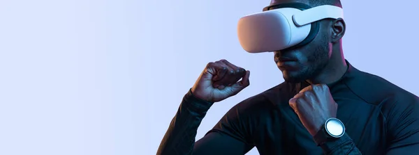 stock image Crop young brutal African American male gamer in stylish clothes and VR glasses boxing against purple background while playing video game
