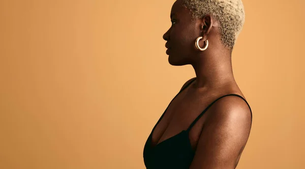 站在橙色背景下 身穿黑色胸罩和耳环的非洲裔美国女性的侧视图 — 图库照片