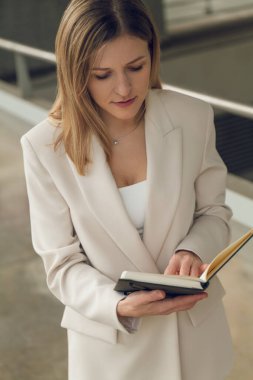 İş toplantısına hazırlanırken bej ceketli yüksek açılı bir iş kadını not defterinden bilgi okuyor.