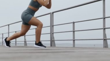 Tanımlanamayan atletik genç bir kadının profil fotoğrafı rıhtımda antreman yaparken atlama hareketleri yapıyor. Kadın dar giysiler içinde egzersiz yapıyor.