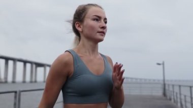 Aktif giyinen atletik bir kızın etrafta koşuşturması, spor yapması. Genç sporcu kadın bulutlu bir günde iskelede kardiyo çalışması yapıyor. Fitness ve motivasyon kavramı.