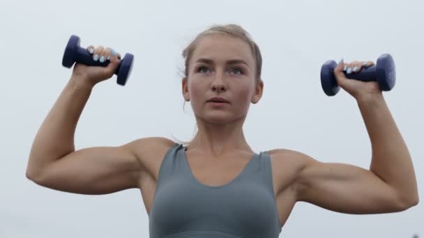 在多云的天气里 强壮健康的年轻女子在户外表演哑铃式的肩膀按压 举重时重点训练女性肌肉 — 图库视频影像
