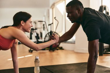 Pozitif sporcu ve Afrikalı Amerikalı eğitmenin spor salonunda çalışırken tahtada el ele tutuşup el ele tutuşmalarının yan görüntüsü